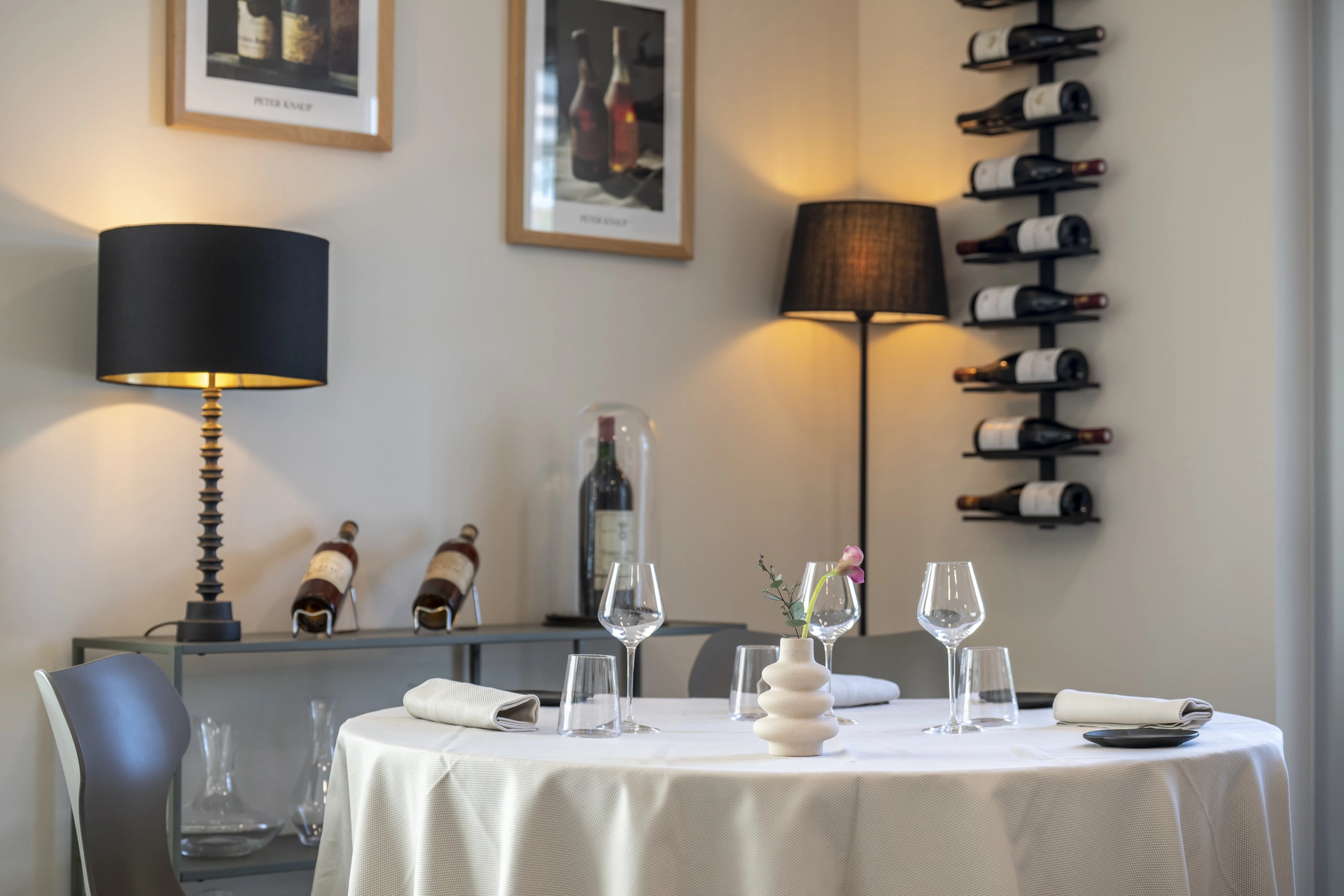 Table ronde dressée pour deux dans l'angle cave à vins de l'Auberge d'Arthaz, lampes noires et nappe blanche