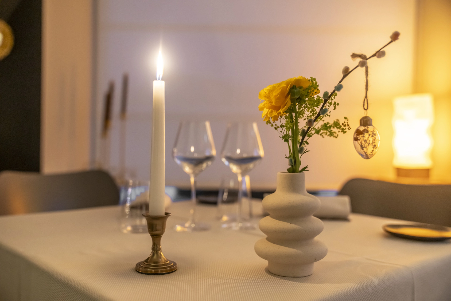 Gros plan sur bougie haute en laiton et vase de renoncules et mimosa, décor de table raffiné à l'Auberge d'Arthaz
