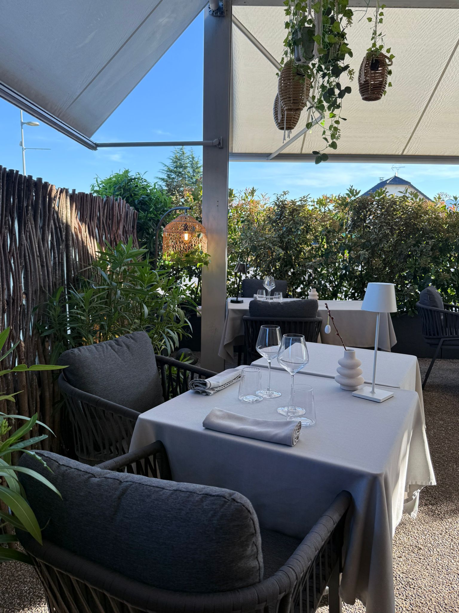 Table pour deux sur la terrasse de l'Auberge d'Arthaz sous ciel bleu franc, paniers osier suspendus et végétation verte