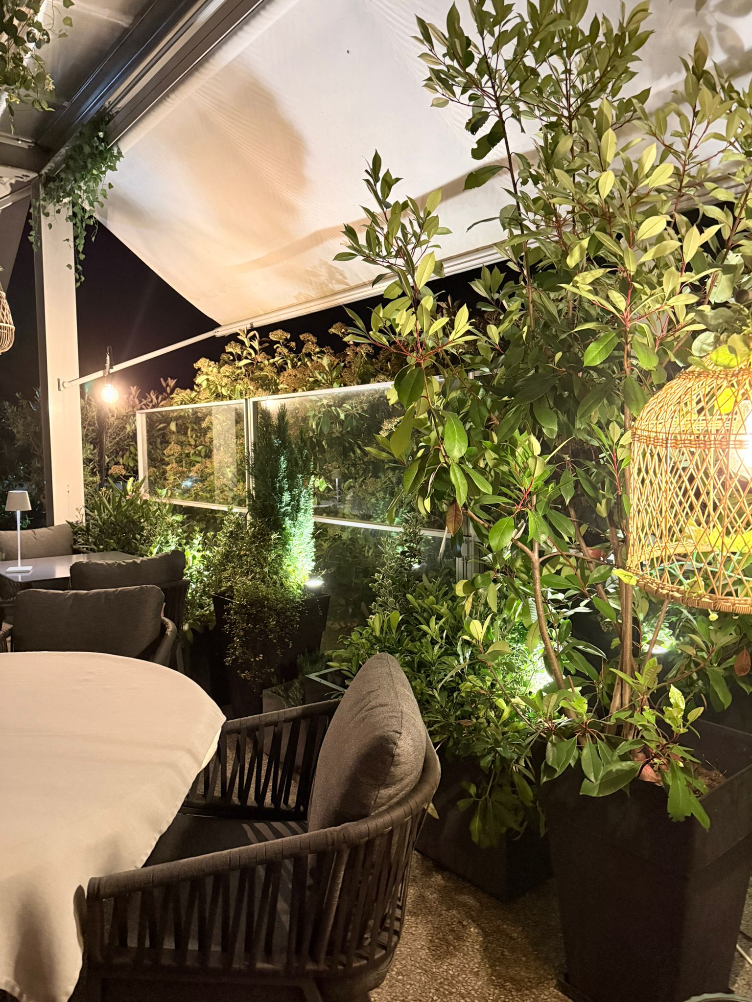 Végétation dense avec magnolia et lierre, fauteuils tressés sur la terrasse couverte de l'Auberge d'Arthaz en soirée